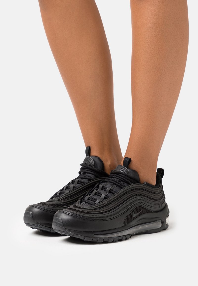 Baskets Nike Air Max 97 noires avec un design ondulé, un tissu texturé, des accents en maille et une unité d'air visible dans la semelle.