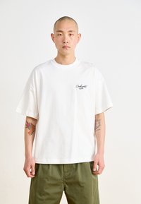 Camiseta de algodón blanca con mangas cortas, cuello redondo y un pequeño logotipo negro de "Carhartt WIP" en el lado izquierdo del pecho. Corte relajado.