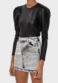 Top negro de manga larga acanalada con hombros abullonados, combinado con una mini falda de mezclilla gris de tiro alto que cuenta con un cinturón y detalles de botones.