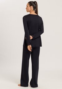 Musta loungemekko, jossa on pitkähihaiset yläosa, jossa on pitsireunukset hihoissa ja kaula-aukossa, yhdistettynä leveälahkeisiin housuihin, pehmeä tekstuuri.