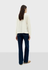 Crème lange mouwen top, relaxte pasvorm, gecombineerd met donkerblauwe rechte jeans en beige slippers. Eenvoudig ontwerp met minimale details.