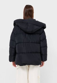 Sort puffjakke med hætte, der har et quiltet design og elastiske manchetter, vist fra bagsiden, med en glat tekstur.