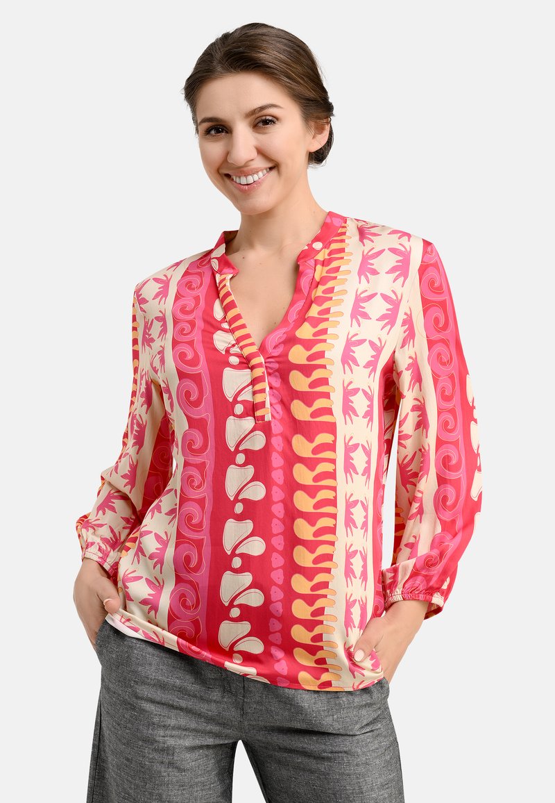 Colorful, patterned blouse in pink, cream, and orange. Long sleeves, V-neck with a button placket, relaxed fit. Soft, smooth fabric.