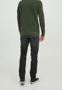 Dunkelgraue Jeans kombiniert mit einem grünen Rippenpullover. Das Outfit zeichnet sich durch ein figurnahes Design und lässige schwarze Sneakers mit weißen Sohlen aus.