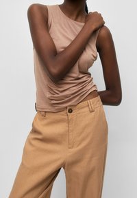 Beżowy dopasowany top na ramiączkach z marszczonymi detalami po bokach, w połączeniu z luźnymi, tanowymi spodniami z pojedynczym zapięciem na guzik oraz fakturowanym materiałem.