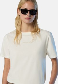 Camiseta de algodón blanca con mangas cortas y cuello redondo, con un sutil logo en beige de "NORTH SAILS" en el frente. Gafas de sol negras.