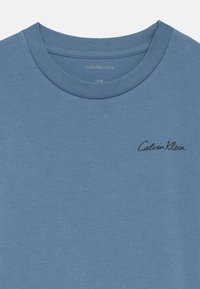 Modrá pánska tričko s okrúhlym výstrihom Calvin Klein s čiernym logom na ľavej hrudi a viditeľnou veľkostnou nálepkou vo vnútri goliera.