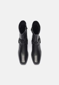 Zwarte leren enkellaarsjes met een gladde textuur, vierkante neus en ritsen aan de zijkant. Voorzien van een decoratieve riem met een gespaccent.
