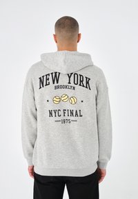 Grå hettegenser med svart tekst "NEW YORK BROOKLYN" og tre gule tennisballer. Ribbestrikkede ermer og nederkant.