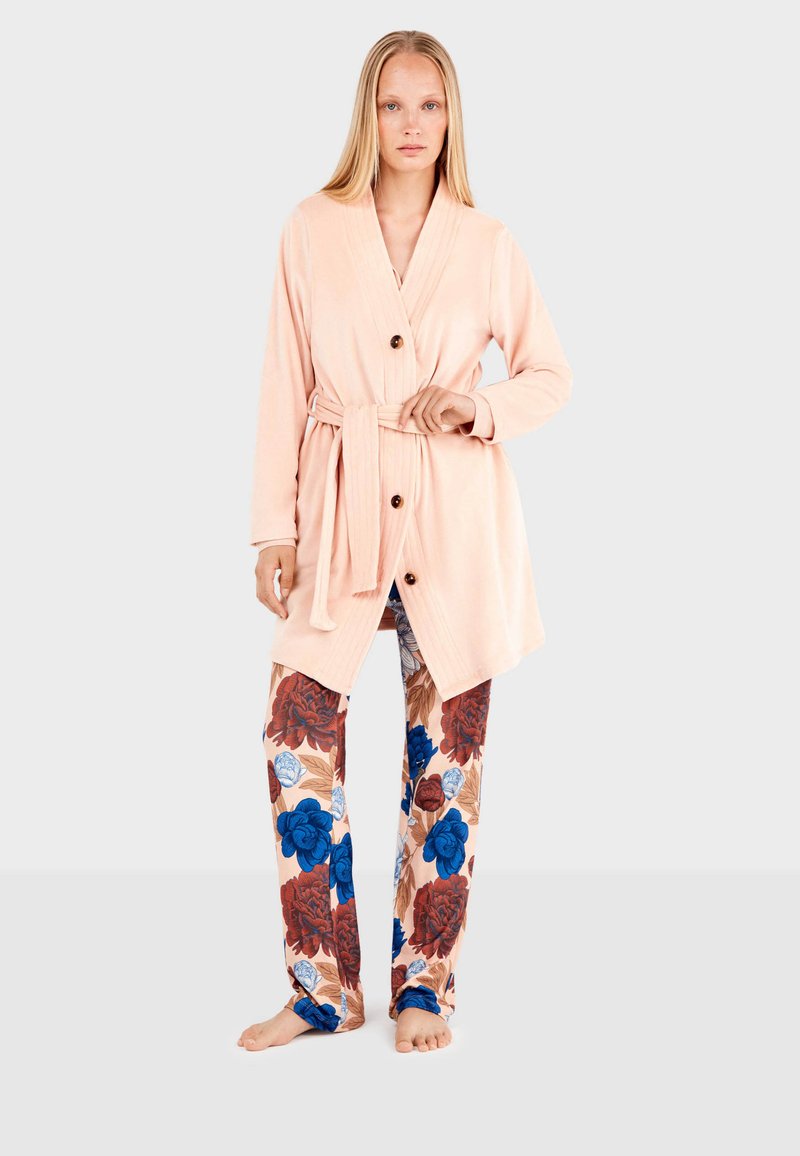 Accappatoio di stoffa morbida rosa con cintura e bottoni in legno, abbinato a pantaloni con fantasia floreale grande in blu e rosso.