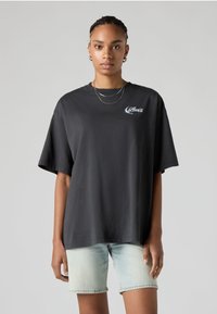 T-shirt preta oversized de algodão com mangas curtas, apresentando um pequeno logo branco da Levi's no peito. Usada com calções de ganga azuis claros.