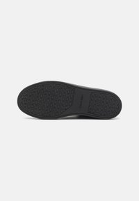 Semelle d'une chaussure noire Calvin Klein avec un motif de semelle présentant des logos "ck" répétés et le nom de la marque dans la zone de la voûte centrale.