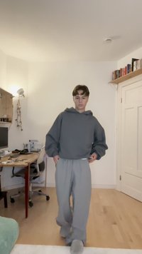 Grijs oversized hoodie met een capuchon, gecombineerd met grijze sweatpants. Glad textiel met een relaxte pasvorm. Scene omvat een thuiskantoor.