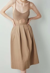 Tan ribgebreide crop top met dunne bandjes, gecombineerd met een beige geplooide midirok. De outfit heeft een getailleerde taille en een zachte textuur.