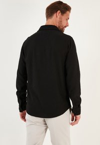 Zwarte geribbelde longsleeve met een opstaande kraag, achterpand en knoopmanchetten, gecombineerd met lichtgekleurde broeken.