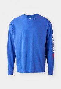 Langarmhemd aus lebhaftem blauen Baumwollstoff. Mit einem Rundhalsausschnitt, bedrucktem Text "OBEY DESIGN" in Weiß entlang des Ärmels und roten Akzenten.