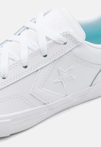 Zapatillas blancas de cuero con un acabado texturizado, que presentan costuras tonales, un logo de estrella y cordones blancos. El forro interior azul añade un contraste.