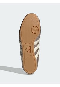 Hnědá podrážka Adidas s rýhami, kruhovým vzorem a světlou gumovou podrážkou s logem Adidas. Design s třemi bílými pruhy.