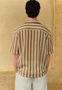 Koszula z krótkim rękawem w paski w odcieniach beżu i brązu, wykonana z teksturowanej tkaniny, z klasycznym kołnierzykiem.