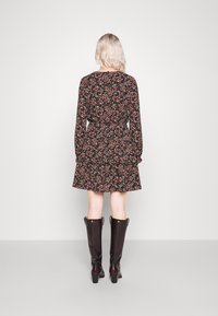 Vestido floral negro con flores rosas y azules, diseño de falda de capas, mangas largas, combinado con botas marrones hasta la rodilla.