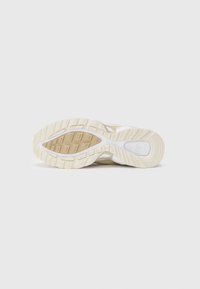 Athletic shoe outsole in a cream color with a textured rubber pattern, featuring a prominent white accent and ridged sections for traction.