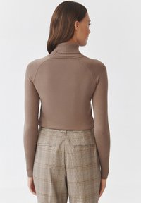 Brązowy dzianinowy sweter z wysokim kołnierzem, o dopasowanym kroju. Połączony z brązowymi spodniami w kratę z wzorem w karo.