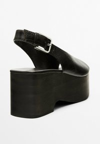 Svarta läderslingbackskor med rundad tå, featuring en tjock plattformshäl och en silverfärgad spänne accent på den justerbara remmen.