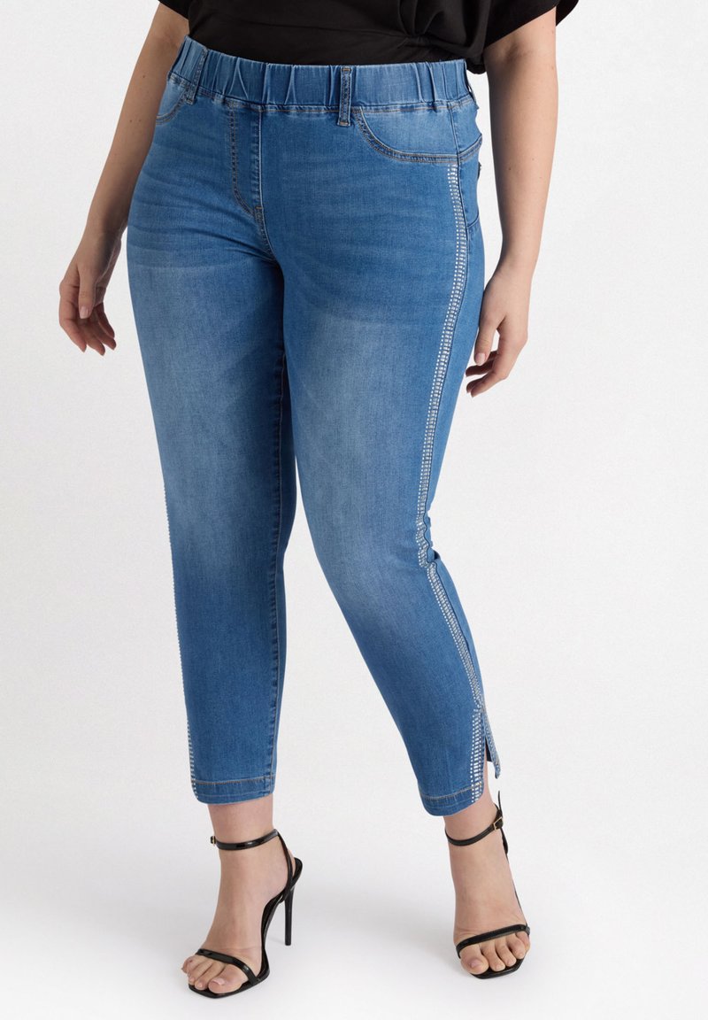 Vaqueros de mezclilla azul con un ajuste tapered, cinturilla elástica y cremalleras laterales. Incluye características como bolsillos y una textura suave.