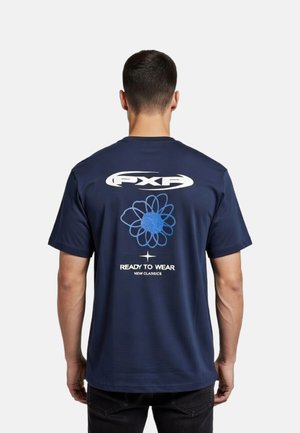 Hombre con una camiseta azul marino con un logo blanco "PXF", una flor abstracta azul y el texto "Ready to Wear New Classics" en la parte trasera.