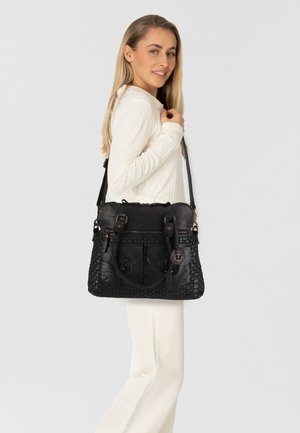 Borsa a tracolla in pelle nera con texture intrecciata, molteplici tasche e dettagli in metallo, mostrata su un modello che indossa un outfit bianco.