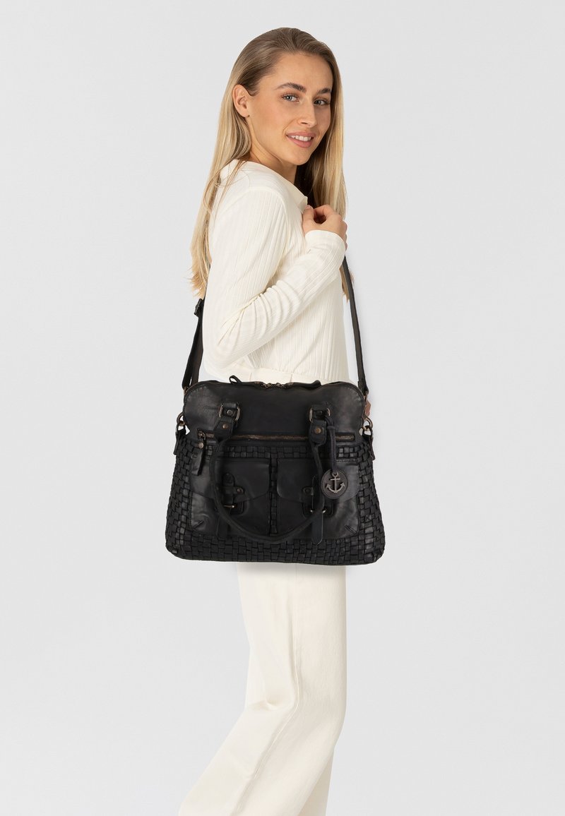 Borsa a tracolla in pelle nera con texture intrecciata, molteplici tasche e dettagli in metallo, mostrata su un modello che indossa un outfit bianco.