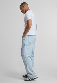 Blugi cargo largi, de culoare albastru deschis, cu buzunare laterale, asortați cu un tricou alb mulat și adidași alb-negru.