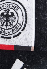 Håndklæde med det tyske fodboldforenings emblem, overvejende hvidt med sorte detaljer, kantet med røde og sorte striber. Struktureret stof.