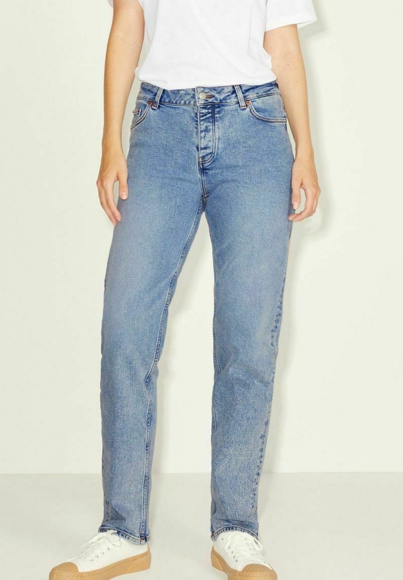 Jeans de ganga azul claro com corte reto, cintura alta, bolsos frontais e um desbotado subtil. Combinados com sapatilhas brancas e uma t-shirt branca.