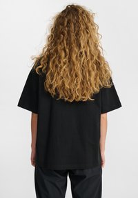 Czarna, oversize koszulka z krótkim rękawem, wykonana z miękkiego materiału. Projekt charakteryzuje się prostym dołem oraz luźnym krojem.