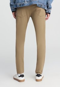 Khaki spodnie o wąskim kroju, wykonane z materiału bawełnianego. Posiadają kieszenie z tyłu i są zestawione z białymi sneakersami z czarnymi akcentami.