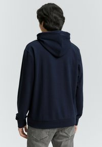 Felpa blu navy con un design sul retro, dotata di cappuccio con coulisse e polsini a costine. Realizzata in materiale morbido, ha una vestibilità rilassata.