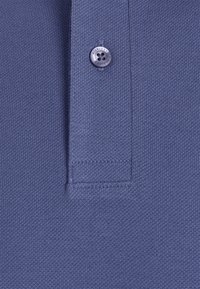 Närbild av en blå stickad polo skjortans knappslå med en enda knapp graverad med texten "Hilfiger".