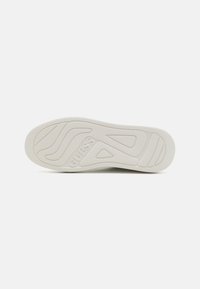 Semelle en caoutchouc blanche pour sneakers, présentant une surface texturée avec des rainures en motifs et un logo "GUESS" embossé au centre.