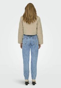 Giacca in pile beige, corta, con texture trapuntata. Abbinata a jeans azzurri chiari a vita alta. Le calzature presentano un tacco scuro e spesso.