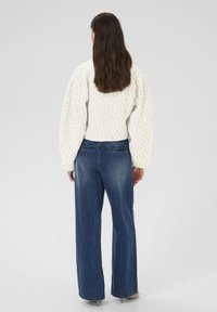 Hvid strikket sweater med lange, voluminøse ærmer kombineret med højtaljede, løstsiddende mørke denimjeans med baglommer.