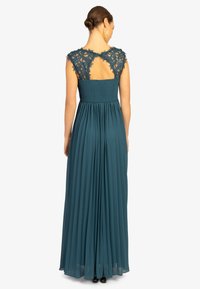 Teal Abendkleid mit plissierter Rockpartie und tailliertem Oberteil. Spitze Puffärmel und ein offenes Rückendetail betonen das Design.