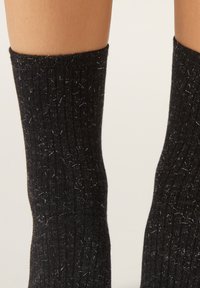 Schwarze Socken mit einer strukturierten Strickoptik, durchsetzt mit hellen Sprenkeln. Der obere Rand ist gerippt und sorgt für eine enge Passform um die Waden.