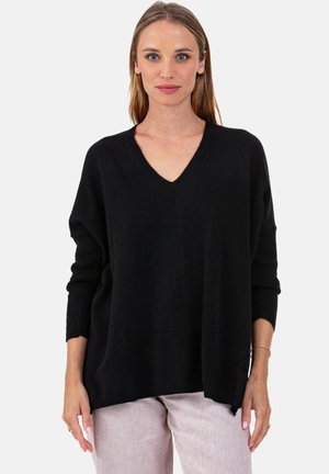 Pull noir à col en V avec une coupe ample, des poignets côtelés et une texture lisse. Associé à un pantalon rose clair, mettant en valeur la silhouette du vêtement.