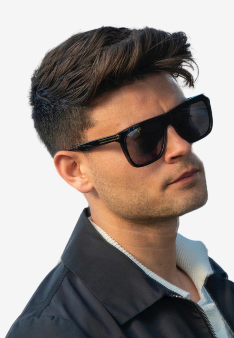 Svarta rektangulära solglasögon med tjocka bågar, bärs av en person. De har en glansig yta och tonade linser. Bakgrunden är helt vit.