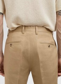Pantalones beige ajustados con dos bolsillos traseros, detalles de botones y trabillas para cinturón; elaborados con una tela suave y un acabado elegante.