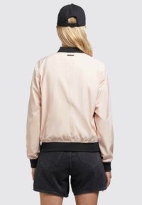 Lichtroze bomberjack met zwarte rand bij de kraag en manchetten. Glad textuur, elastische tailleband en labeldetail op de achterkant. Gepaard met zwarte shorts.