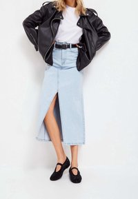 Dżinsowa spódnica midi z przednim rozcięciem, jasnoniebieska, zestawiona z czarną skórzaną kurtką motocyklową i czarnymi butami z ćwiekami.
