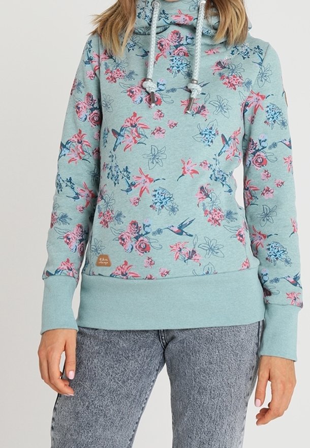 Sweat à capuche bleu clair avec motifs floraux et oiseaux roses et bleus, cordons blancs et col montant, porté avec un jean gris délavé à l’acide.