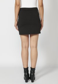 Černá mini sukně s hladkou texturou a přiléhavým střihem. Obsahuje detail s bočním akcentem. Kombinována s černými kotníkovými botami na podpatku.